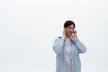 Mavi gömlekli ve kulaklıklı gözlüklü neşeli, genç bir doğu kadını. Ellerini üstünde tutuyor, müzikten hoşlanıyor. Beyaz arka planda izole edilmiş. Müzik dinliyordum. Dizinin bir parçası.