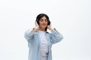 Mavi gömlekli, kulaklıklı neşeli, genç bir doğu kadını. Ellerini üstünde tutuyor, müzikten hoşlanıyor. Beyaz arka planda izole edilmiş. Müzik dinliyordum. Dizinin bir parçası.