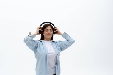 Mavi gömlekli, kulaklıklı neşeli, genç bir doğu kadını. Ellerini üstünde tutuyor, müzikten hoşlanıyor. Beyaz arka planda izole edilmiş. Müzik dinliyordum. Dizinin bir parçası.