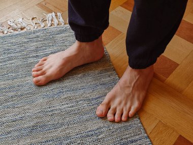 Halıdaki adamın bacaklarının görüntüsünü kapat. Siyah pantolonlu bacaklar, rahat ev atmosferi. Pediatrist ve tıp medyası için içerik. Saçlı insan ayakları..