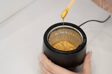 Altın cilasını tüy dökümü için ısıtmak ve elleri tek kullanımlık eldivenlerde tutmak için bir cihaz. Kişisel bakım, güzellik endüstrisi, tüy dökücü, balmumuyla tüy dökücü. Metnin için alanı kopyala. Yatay.