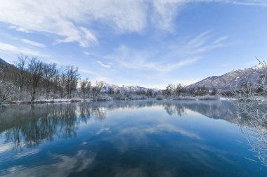 Mavi gökyüzü ve ağaçlarla çevrili karlı ve göllü kış manzarası