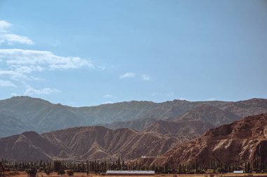 Göz kamaştırıcı bir sıradağ canlı mavi bir gökyüzüne karşı kurulmuş, ön planda belirgin şekilde yemyeşil ağaçlar sergilenmiş, resim gibi bir manzara yaratıyor.