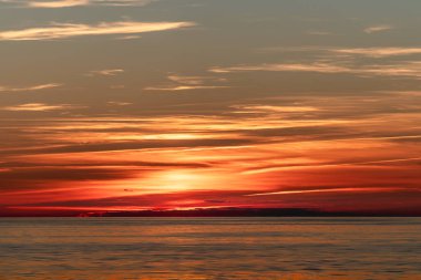 Işıl ışıl güneş, sakin bir su kütlesinin üzerinde güzelce batıyor. Gün geceye geçerken gökyüzünde canlı renkler bırakıyor.