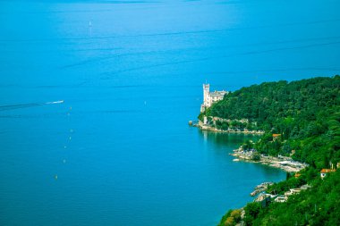 Görkemli bir şato zarif bir şekilde yüksek bir tepenin üzerinde duruyor. Aşağıdaki suyun sakin ve görkemli gövdesine bakıyor.