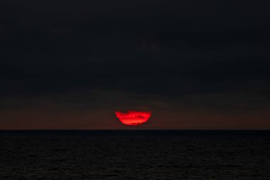 Gün sona ererken güneş yavaşça engin okyanusa batıyor ve batarken sıcak renkleriyle bulutlu gökyüzünü boyuyor.