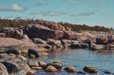 Berrak mavi gökyüzünün altında sakin sularla buluşan kayalık bir kıyı şeridinin nefes kesici manzarası mükemmel bir manzara yaratıyor.