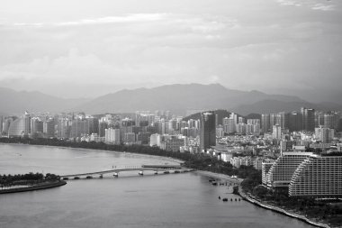 Çarpıcı bir siyah beyaz manzara, bir kıyı şehrini yakalar, dağlık bir zemin karşısında modern mimariyi sergiler.