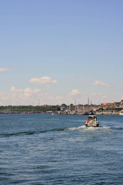Güzel mavi gökyüzünün altında huzurlu bir kıyı şeridi tarafından çerçevelenmiş, sakin sularda süzülen küçük bir tekne.