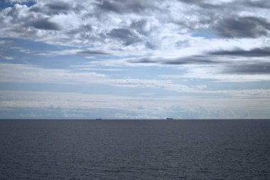Okyanusun sakin bir görüntüsü gökyüzü ile buluşuyor, dağınık bulutlar sahneleri ve derinliği artırıyor.