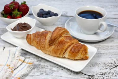 Beyaz bir ahşap üzerinde bir fincan kahve ve kruvasan.