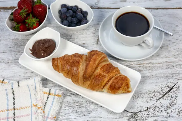Beyaz bir ahşap üzerinde bir fincan kahve ve kruvasan.