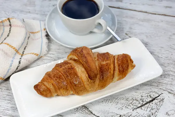 Beyaz bir ahşap üzerinde bir fincan kahve ve kruvasan.