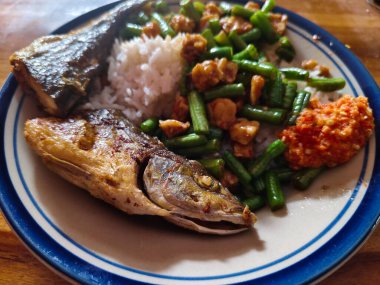 Lezzetli bir Endonezya yemeği ızgara balık, pirinç, tofulu yeşil fasulye ve ahşap masada baharatlı sambal.