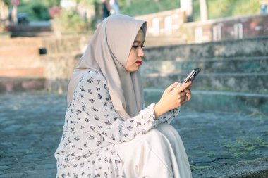 Modern tesettür giyen Asyalı kadın parkta akıllı telefonunu kullanarak sosyal medyada oynuyor - Asyalı kadın