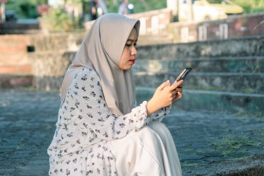 Modern tesettür giyen Asyalı kadın parkta akıllı telefonunu kullanarak sosyal medyada oynuyor - Asyalı kadın