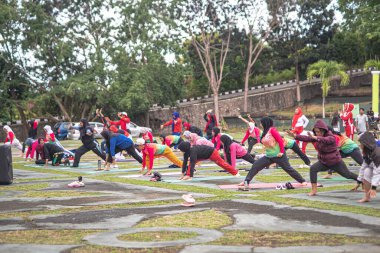 Indonesia, 29 June 2024 - A group of women are doing yoga in the park - Group of diverse women doing yoga exercises together in park in summer and having fun clipart