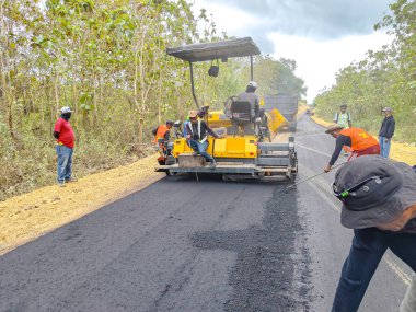 Baubau, Endonezya, 30 Kasım 2024 - İnşaat İşçileri Kırsal Yolları İnşa etmek için Ağır Ekipman Kullan - Asfalt kaldıracı, yol yüzeylerine sıcak asfalt karışımı yaymak, düzleştirmek ve sıkıştırmak için kullanılan ağır bir ekipmandır.