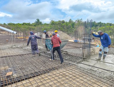 Baubau, Endonezya, 30 Kasım 2024 - İnşaat işçileri döşeme döşemeleri için beton dökerler - İnşaatçı inşaat halindeki bir evin zemin katına takviye levha dökerken geniş bir hortumdan taze beton akar.