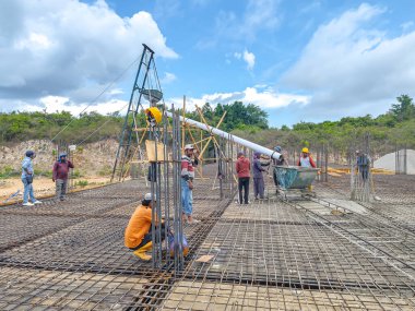Baubau, Endonezya, 30 Kasım 2024 - İnşaat işçileri döşeme döşemeleri için beton dökerler - İnşaatçı inşaat halindeki bir evin zemin katına takviye levha dökerken geniş bir hortumdan taze beton akar.