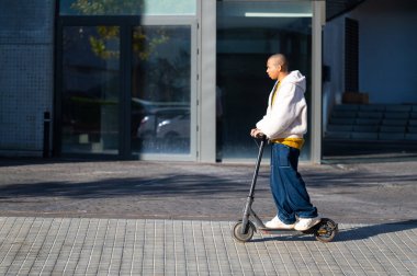 Modern bir şehirde scooter 'ı sürdürülebilir ulaşım yöntemi olarak kullanan şık bir insan.