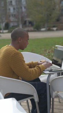 Yanında elektrikli scooterıyla parkta bir bankta otururken dizüstü bilgisayarı üzerinde çalışan genç bir serbest çalışan.