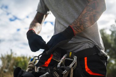 Ağaç budamaya hazırlanan eldiven ve koşum takımı giyen halat erişim teknisyeni.
