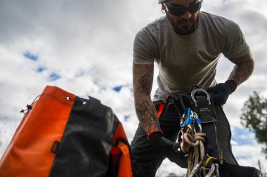 Worker wearing safety harness checking climbing equipment before starting tree pruning work clipart