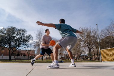 Güneşli bir günde sokakta basketbol oynayan iki arkadaş, dostça bir yarışmanın tadını çıkarıyorlar.