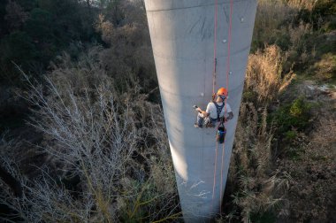 Beton baca üzerinde çalışan halat erişim teknisyeni, bakım veya teftiş için demirleme yerleri kuruyor