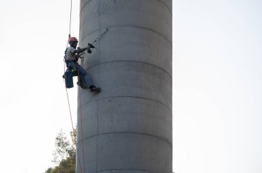 Elektrikli matkap kullanarak beton bacaya demir döşeyen endüstriyel dağcı.