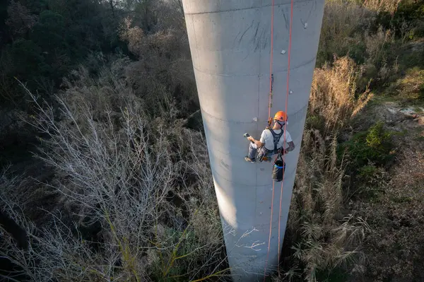 Beton baca üzerinde çalışan halat erişim teknisyeni, bakım veya teftiş için demirleme yerleri kuruyor