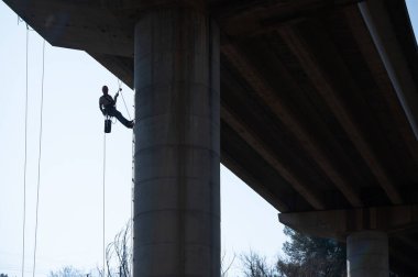 Halat erişim teknisyeni iplerden sarkan beton köprü sütunlarını inceliyor.