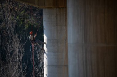 Endüstriyel tırmanışçı köprü sütununu ipler ve özel ekipmanlarla inceliyor.