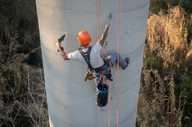 Beton baca üzerinde çalışırken matkap kullanan endüstriyel tırmanışçı.