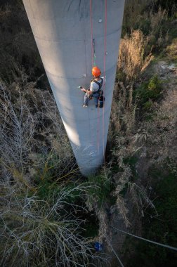 Endüstriyel tırmanışçı beton köprü direğinden sarkıyor.