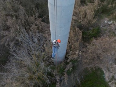 Endüstriyel tırmanışçılar beton bir bacadan iple iniyorlar, kırsal alanda teftiş ve bakım çalışmaları yapıyorlar.