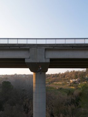 Beton bir köprünün altında çalışan endüstriyel tırmanışçı, bakım ve teftiş görevlerini yerine getiriyor