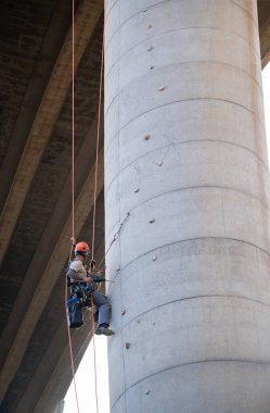 Endüstriyel tırmanışçı beton köprü sütununda denetim ve bakım yapmak için halatlar kullanıyor.