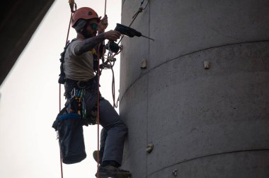 Beton bir bacada çalışırken döner çekiç matkabı kullanan bir adam.