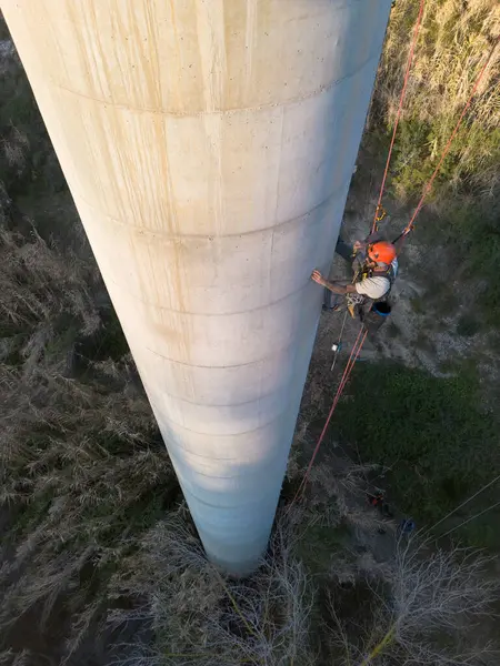 Yüksek beton bacayı kontrol eden adam çift halat giriş tekniği kullanıyor, güvenlik ve bakım sağlıyor.