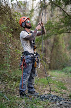 Kask ve koşum takımı giyen profesyonel endüstriyel tırmanıcı, bir yapıya tırmanmak için ipler hazırlıyor, güvenlik ve uzmanlık gösteriyor