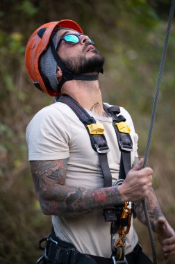 Kask ve koşum takımı takan işçiler halata tırmanırken yukarı bakarlar.