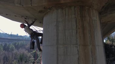 Uzman işçiler, beton köprü sütununu tamir etmek için iplerden sallanıyorlar.