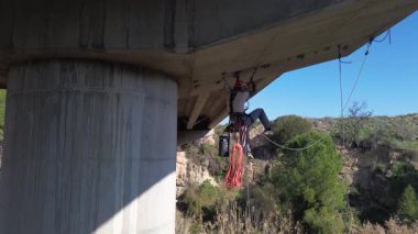 İnşaat işçisi, beton köprünün altını inceleyen iplere asılmış.