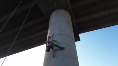 Profesyonel halat erişimi. Beton köprü sütununu dikkatlice incelemek. Uzman güvenlik ekipmanları ve teknik uzmanlık kullanılarak yükseklikten askıya alınmış.