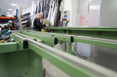 Marangoz alüminyum profiller üzerinde yoğunlaşıyor, hareketli bir atölye ortamında çalışan makineler