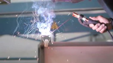 İşçi elektrot kullanarak metal parçaları kaynak yapar, atölye ortamında kıvılcım ve duman yaratır