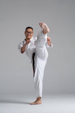 Kyokushinkai 'li bir karate dövüşçüsünün tam boy portresi. Gri bir arka planda beyaz bir elbise ve siyah kuşak takıyor.