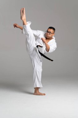 Kyokushinkai karate dövüşçüsü beyaz keikogi ve siyah kuşak giyerek gri zemine güçlü bir tekme atıyor.